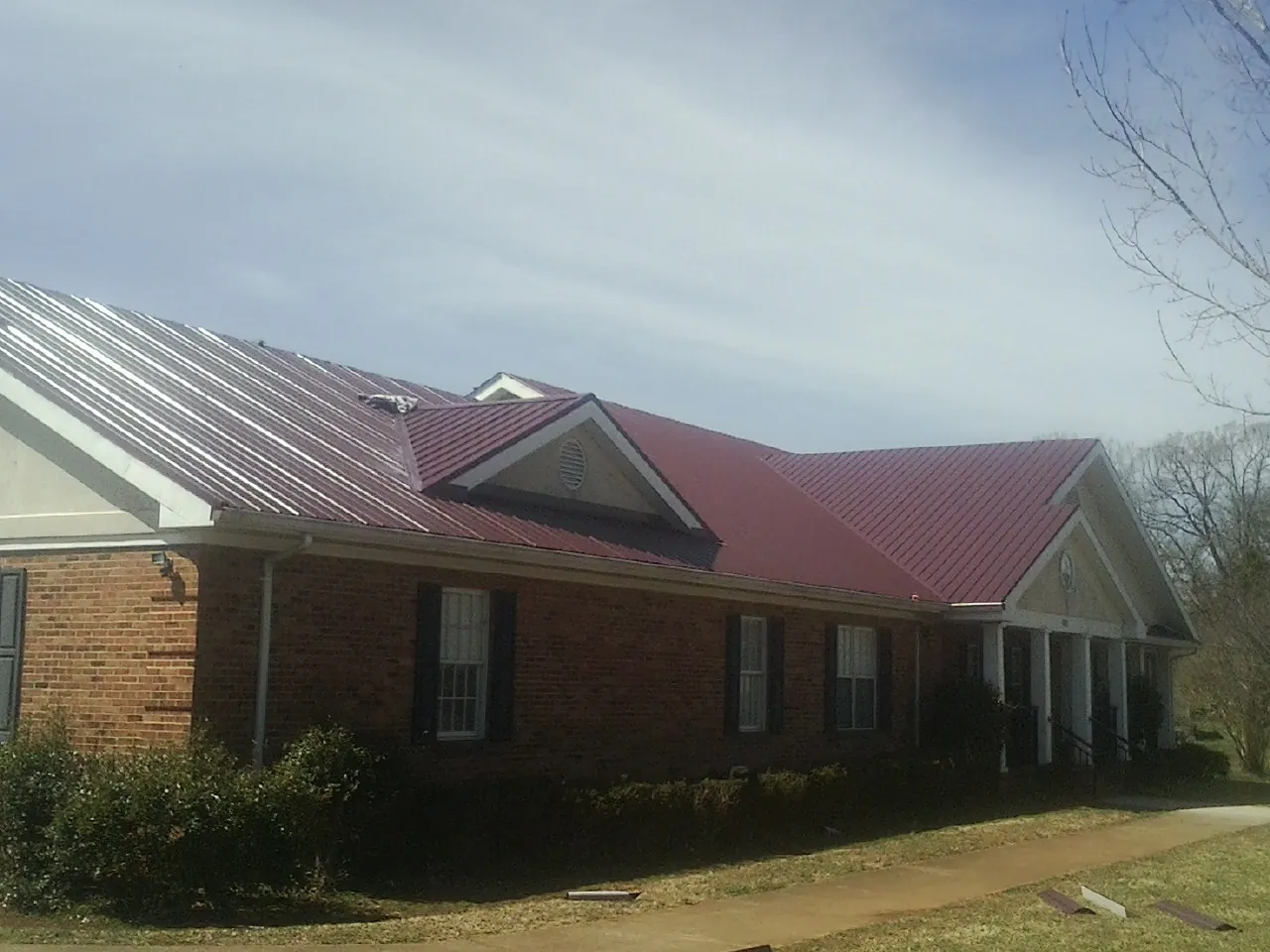 Red metal roof with gabled entries on a long brick building, from a Hail Damage Roof Repair job in Irwin